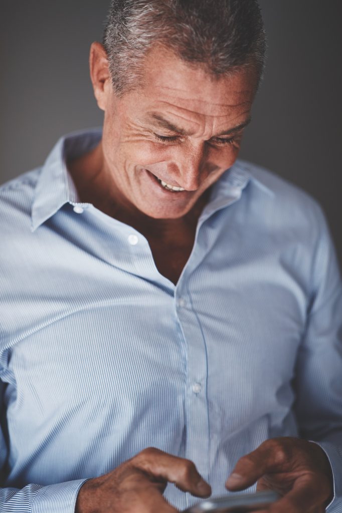 Smiling mature businesman standing against a gray background reading texts
